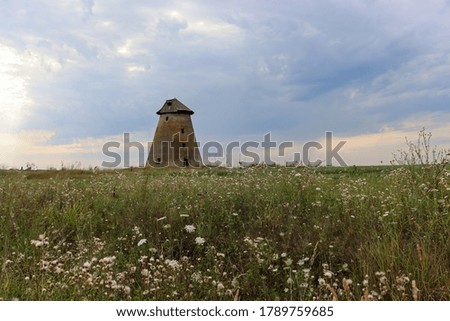 Ruined vintage windmill in the meadow on rainy, summer evening. Beautiful countryside landscape