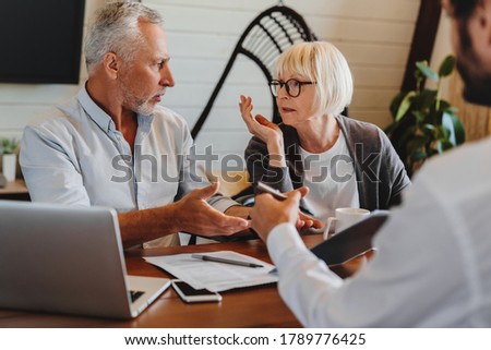 Financial advisor giving retirement advice to old couple while they arguing at home interior Royalty-Free Stock Photo #1789776425
