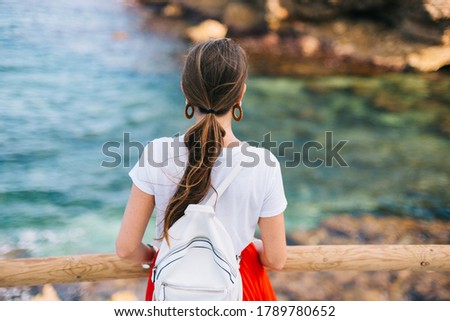 A girl in a red dress escorts the sunset to the sea. Horizontal photo banner for website header design with copy space for text. Back view of a woman.
