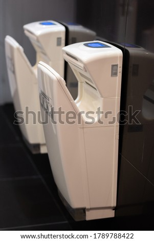 Two white electrical hands dryers in public bathroom against the black wall, contrast