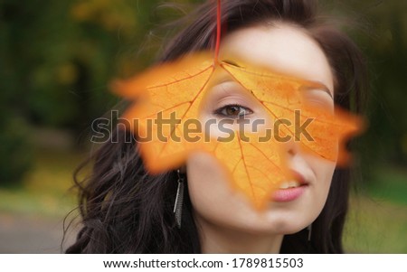 Autumn woman holding yellow maple leaves and hiding her eye. Cute female model looks out of yellow leaves. Happy  smiling blond teen girl with autumn leaf in the heart form