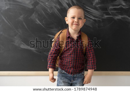 Portrait of a schoolboy boy who is standing in front of the blackboard and smiling. The blackboard is clean with traces of chalk. The child is dressed in a dark shirt and jeans. The concept of