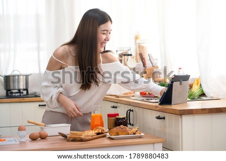 Young Asian woman prepare for breakfast in kitchen, using digital tablet computer, hand touch on tablet  Royalty-Free Stock Photo #1789880483