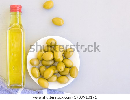 A glass bottle of olive oil, a bowl of olives, and a towel. Grey background, space for text.