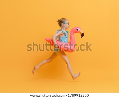 Happy child wearing swimsuit. Girl with swimming ring flamingo. Kid on a colored yellow background.