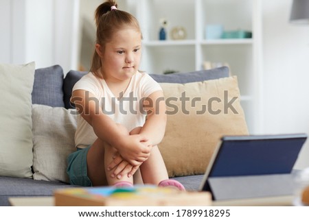 Down syndrome girl sitting on sofa and watching movie on digital tablet in the living room at home Royalty-Free Stock Photo #1789918295