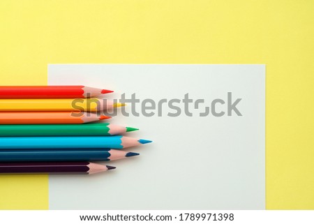 Colorful pencils on white paper on yellow background, flat lay, close-up. Set of rainbow pencils, copy space. Pencils are sharp.