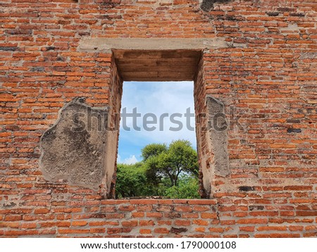 A window on brick wall that can see through and there is branch of tree with blue sky. Perspective view in historical place in Ayutthaya, Thailand.