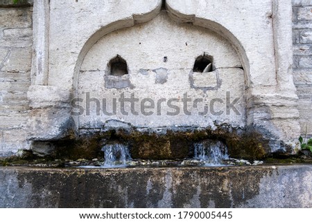 Front Close Up of Stone Drinking Fountain with water from the middle ages with blurry water