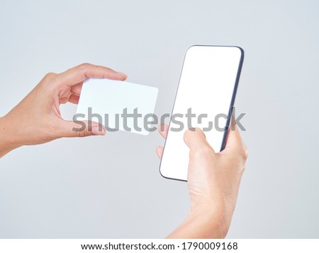 Mock-up image of woman hand holding mobile phone, blank screen and credit card on gray background