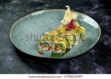 Japanese sushi rolls with eel and avocado in a blue plate on a black background. Roll green dragon