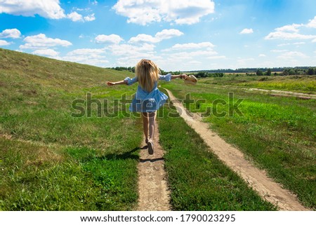Back view of  young girl in blue dress running at along the trail