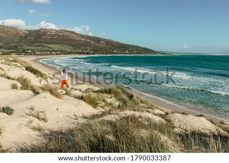 Joyful happy girl jumping on a beach on a bright summer day.Majestic view of wild sandy beach,waves and seashore.Female traveler enjoying her holiday.Lust for life scene. Wanderlust travel background. Royalty-Free Stock Photo #1790033387