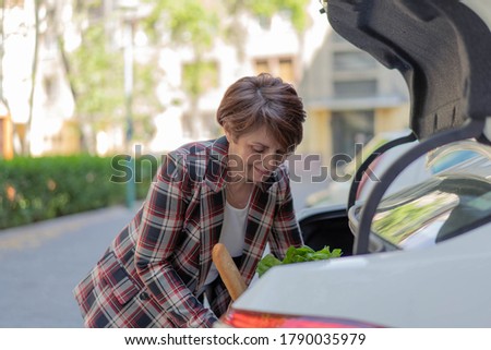Woman taking out her shooping bags from car at parking lot. 