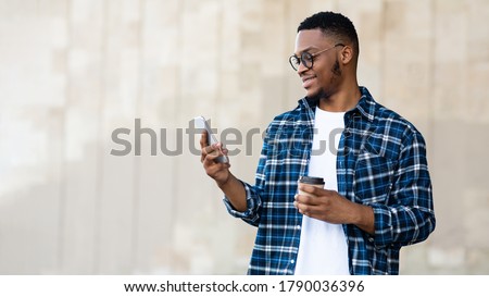 Technology Concept. Young successful afro designer reading good news from friends on phone and enjoying morning coffee