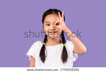 Korean Little Girl Looking Through Okay Sign Covering Eye Posing On Purple Studio Background. Everything Is OK. Free Space