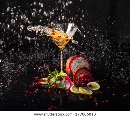 Colorful splash in martini glass from falling lemon, with pomegranate seeds, slices of dragon fruit, green apple, oranges and lemons, on a wet black table
