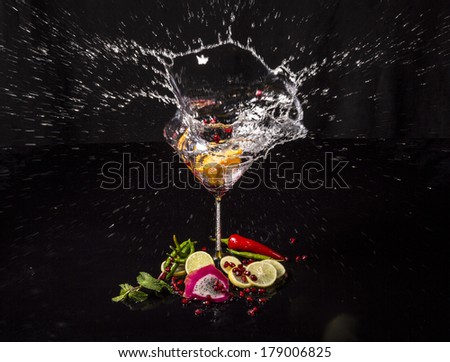Colorful round splash in martini glass from falling lemon, with pomegranate seeds, slices of dragon fruit, green apple, oranges and lemons, on a wet black table