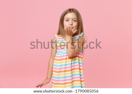 Lovely little fun female kid girl 5-6 years old in colorful dress blue eyes send air kiss isolated on pink background children studio portrait. People childhood lifestyle concept. Mock up copy space.