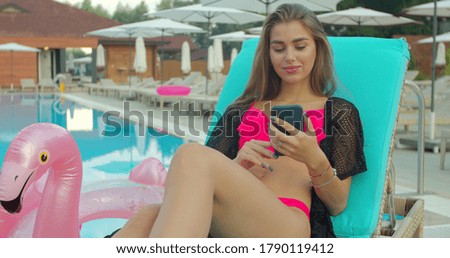 Summer woman using mobile and sunbathing at swimming pool. Woman sunbathing with mobile phone.