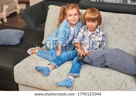 Happy little brother and sister watch TV, holding a remote control. family life at home. Happy childhood. Family at home.