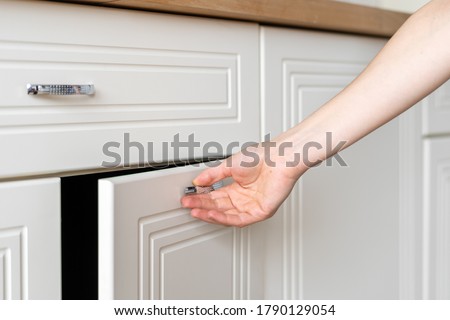 Cropped view of woman hand open door at cupboard furniture standing on modern kitchen at home with white interior Royalty-Free Stock Photo #1790129054