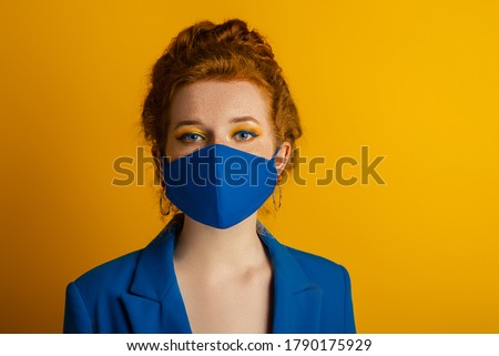 Redhead woman wearing trendy fashion blue monochrome outfit with  protective face mask. Model has matching bold eyes makeup. Style during quarantine of coronavirus outbreak. Copy, empty space for text