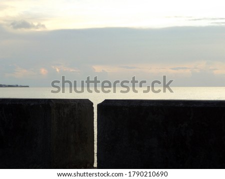Beyond the seawall is a reflection of the sunset on the sea in addition to contrasting tones in the sky