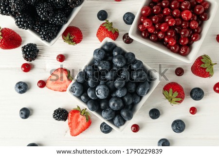 Bowls with berries on white wooden background, top view