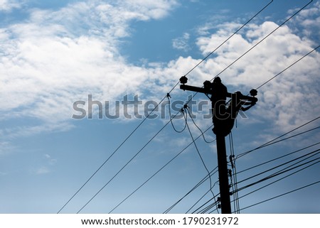Silhouetted electricians working at electric pole in blue sky background