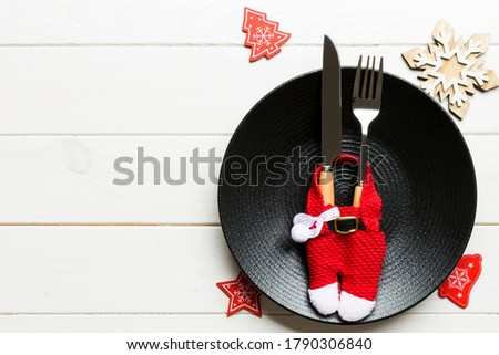Holiday composition of plate and flatware decorated with Santa clothes on wooden background. Top view of Christmas decorations with empty space for your design. Festive time concept.