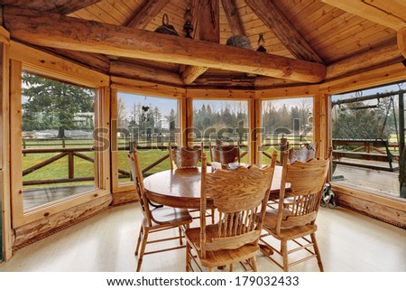 Bright dining room in log cabin house with floor-to-ceiling windows, rustic dining table set and cathedral ceiling with beams.