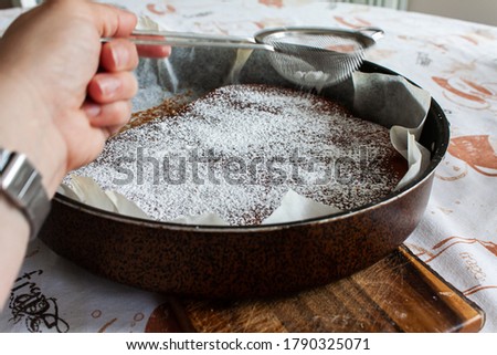 Home baking. Sprinkling icing sugar with a sieve on a cake ready got out of the oven, still warm. 