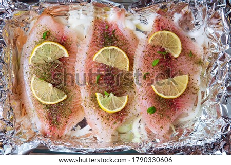 Raw tilapia fillet with lemon and spices close up in baking foil