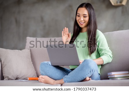 Full length photo of positive girl korean social media blogger sit couch legs crossed use laptop have online live broadcast wave hand in house indoors
