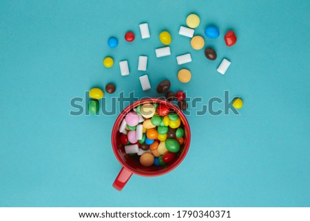 Many multi-colored sweets in a red mug, a turquoise background