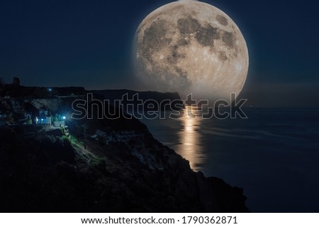 The full moon rises in a starry night sky over the sea and rocky cliffs. The concept of calmness, silence and unity with nature.