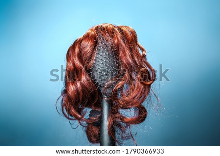 Females hair. Black hairbrush with a red wig, looks like a woman's head with a hairstyle. Blue background. Copy space. Concept of beauty salon, hair care and hair transplant Royalty-Free Stock Photo #1790366933