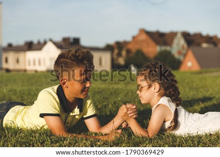 young brother and sister lying on the grass wrestle in their arms