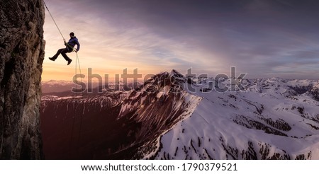 Epic Adventurous Extreme Sport Composite of Rock Climbing Man Rappelling from a Cliff. Mountain Landscape Background from British Columbia, Canada. Royalty-Free Stock Photo #1790379521