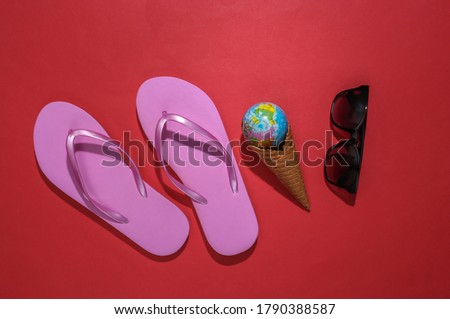 Flip flops, ice cream waffle cone with globe, sunglasses on red background. Summer flat lay. Top view