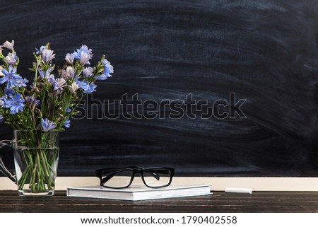 Flowers in a glass cup, glasses, against the background of chalkboard, Teacher's Day concept. Copy space.
