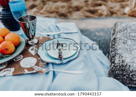 Beautiful decoration of wedding picnic on the beach with oranges, glas of vine, blue plate with lavendar and pillows. Outdoor marriage photography, Crete Greece.