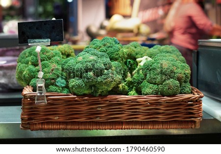 Wicker basket with fresh green bundles of broccoli in a shop window with a black signs price against the background of a supermarket interior with blurred background and bokeh.