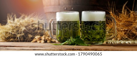 Green beers on a wooden table, in the back of the original oak barrel and wheat cob. This beer is traditionally served on St. Patrick's Day, or also during Easter times in Europe. Wide banner panorama