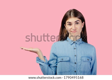 Indifferent woman dressed in casual outfit spread hands sideways, have no idea, pose against pink color background. Confused questioned girl with clueless expression indoor. Copy space.