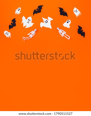 Black paper bats, white ghosts and rubber skeletons flying on top of orange cardboard. Halloween vertical background, copy space