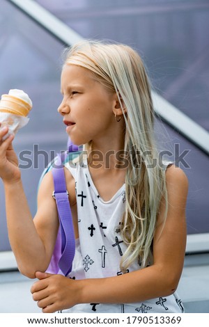beautiful girl with long blond hair with ice cream in a cone, summer day in the city. Child with ice cream in a cone.