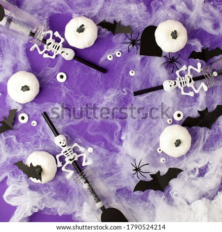 Halloween decorations. Decorative white pumpkins, bats, eyes, bottles with creepy straws for cocktail on purple background. Halloween party concept. Flat lay, top view, copy space, square