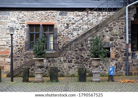 An old stone house with a metal staircase and with plants in clay pots in front of it